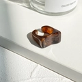 Detailopname van amberkleurige harsring met uniek onregelmatig design op witte achtergrond - Amber Bruin Patroon (5305102)