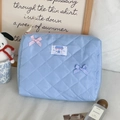 Detail of blue quilted cosmetic bag featuring soft fabric and decorative bow accents - Blue Hand Pouch