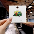 Vista dettagliata di una spilla smaltata colorata a forma di camper su cartoncino bianco - Camper a Fumetti