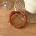 Brazalete ancho irregular de resina ámbar marmoleada sobre fondo de mesa de madera - Diámetro Interior 6,5 cm / Patrón de Carey Ámbar