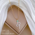 Macro view of gold snake pendant with green gem eyes and crystals on silk background - Gold
