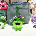 Détail du porte-clés monstre en peluche vert fluo attaché à un sac en jean bleu - Vert