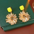 Detailaufnahme der goldenen Ohrringe mit Kristallblume und grünem Edelstein auf Box - Goldbraun