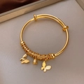 Détail d'un bracelet doré avec des breloques de muguet et de papillon élégant - Style Papillon Muguet / Doré