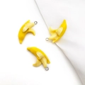 Three yellow peeled banana acrylic pendants for DIY jewelry making on white fabric - Banana
