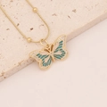Elegant gold butterfly necklace with green and white enamel on beige stone surface - Green