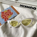 Detail shot of white cat-eye sunglasses with yellow lenses on a white textured background - Cat Eye / White Frame Yellow Lens
