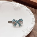 Detail of blue rhinestone bow hair clip on a white vintage plate with duckbill clip - Bow / Green