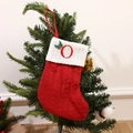 Red knitted Christmas stocking with embroidered letter O and holly leaf hanging on a tree - Letter O