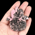 Hamsa Hand carving in pink and black rhodonite stone held in hand on black background - Rhodonite
