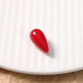 Macro view of a smooth red teardrop-shaped resin bead on a white textured ceramic tray - 1 Piece / Red