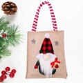 Christmas burlap gift bag with gnome pattern and red striped handles on white wood - Santa Claus Gift Tote Bag