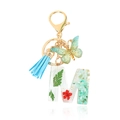 Letter M resin keychain with green dried flowers and blue tassel on white background - Letter M