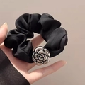 Elegante coletero de seda negra con un dije de flor de camelia plateada sobre fondo beige - Camelia de Plata