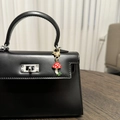 Détail d'un pendentif champignon rouge à pois blancs sur un sac à main en cuir noir - Champignon Feuille Verte Fraise