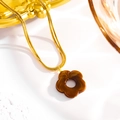 Macro view of gold snake chain with amber-textured flower pendant on white scene - Coffee