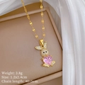 Detail of a gold bunny necklace with pink heart stone and crystals on a beige jewelry box - Pink Rabbit Necklace (E325)
