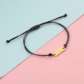 Detalle de la pulsera de cuerda trenzada negra ajustable con una placa rectangular de metal dorado - Cuerda Negra Dorada