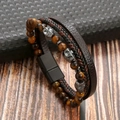 Dettaglio di un bracciale multistrato da uomo in pelle con perline occhio di tigre e teschi - Caffè + Occhio di Tigre