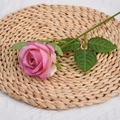 Artificial pink rose with green leaves and stem on a woven straw mat backdrop - Gradient Purple