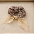 Brown plaid fabric scrunchie with a beige translucent ribbon bow on textured cloth - Brown