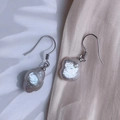 Detailed macro view of irregular baroque pearl earrings with silver ear hooks on satin - Silver Four-Leaf Clover