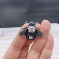 Silver bee brooch with black and white rhinestones held between fingers for size - Style 23