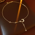 Detail van gouden Y-ketting met zirkonia ster- en maanhangers op lederen achtergrond - Goud