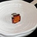 Macro detail of large square orange gemstone set in a polished silver ring mount - Brown