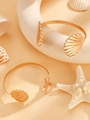 Set de pulseras doradas con dijes de estrella de mar y conchas sobre fondo beige - Set de 2 Piezas Brazalete de Estrella de Mar y Concha
