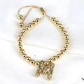 Detailed close-up of a golden beaded bracelet with a zircon-inlaid letter M pendant - Letter M