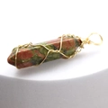 Unakite hexagonal prism pendant wrapped in gold wire on a white display pedestal - Unakite
