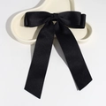 Close-up of elegant black satin bow hair clip with long ribbon on a ceramic plate - Black