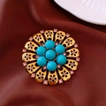 Makroaufnahme einer Vintage-Goldbrosche mit türkisfarbenen Perlen und rosa Strass - Goldene Hohlblumenbrosche - Blaue Perlen Rosa Strass