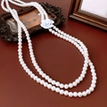 Elegante dubbellaagse lange parelketting met witte camelia hanger op een lederen achtergrond - Witte dubbellaagse parelketting met camelia