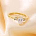 Makroaufnahme von Gold-Edelstahlring mit birnenförmigem Zirkon auf champagnerfarbener Seide - US 6 / Gold mit klarem Hauptstein (KR111193-TOM)