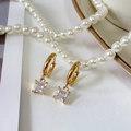 Macro detail of gold-plated square zircon earrings resting on white pearls and porcelain - Clear
