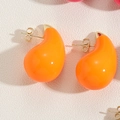 Macro view of teardrop enamel stud earrings in bright orange with golden metal backings - Orange