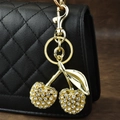 Gold cherry keychain with sparkling crystals attached to a black quilted handbag - Rhinestone Cherry Gold Leaf White