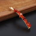 Macro shot of gold bobby pin with red agate stone fragments on a dark wooden tray - Red Agate Gold