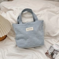Detail of light blue denim tote bag with white bow embroidery and canvas studio label - Light Blue