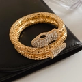 Close-up of golden snake wrap bracelet with crystal-pave head and textured metal finish - Gold