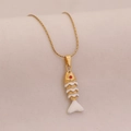 Detailed close-up of golden fish pendant with white enamel and red gemstone eye on a fine chain - White