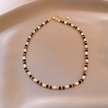 Détail du collier de perles en œil de tigre et perles dorées sur un fond de soie douce - Collier de Perles de Coquille Oeil de Tigre Plaqué Or 18K