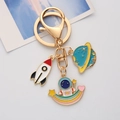 Close-up of golden astronaut keychain with rocket and planet charms in enamel finish - Rainbow Astronaut / Single OPP Bag Packaging