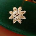 Dettaglio macro della spilla a fiocco di neve dorata con zirconi su velluto verde scuro - Oro (Placcato Oro Vero)