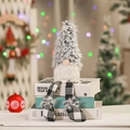 Gnome de Noël en peluche à longues jambes assis sur des livres devant un sapin festif - Petit Carreaux Gris / Petit