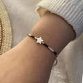 Detail of shell star charm on beaded bracelet with black and gold beads worn on wrist - Black
