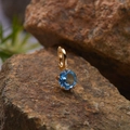 Detail of a blue gemstone pendant in gold plating resting on a natural brown stone - Natural Topaz Round Pendant Gold