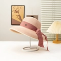 Détail d'un chapeau de paille beige avec ruban rose et badge métallique doré 'M' - Rose